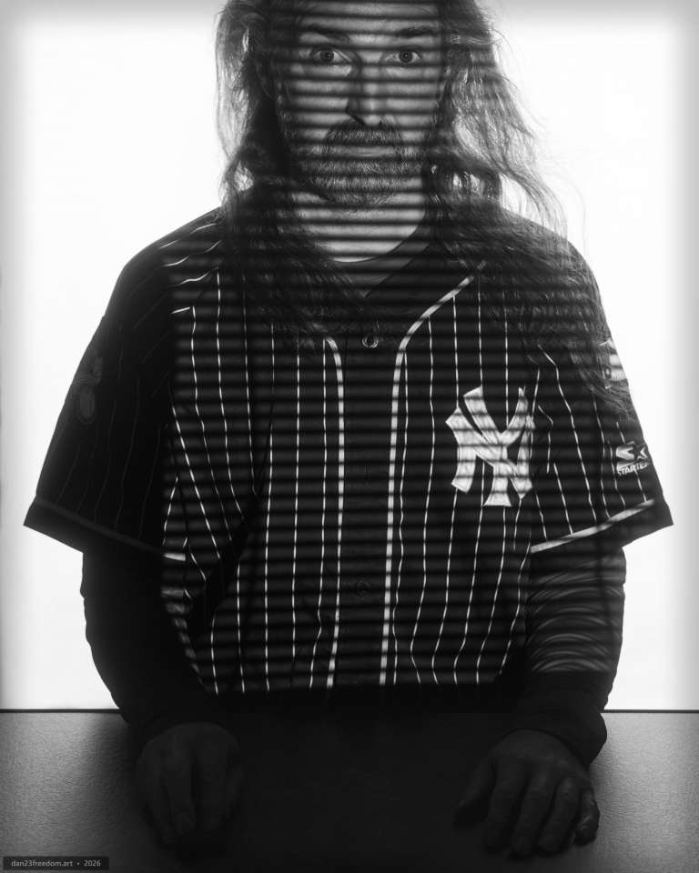 A seated self-portrait with horizontal bands of shadow across the face, hair and pinstripe Yankees jersey against a bright background.