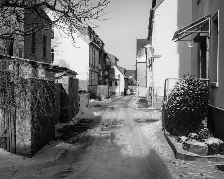 Two figures walk down a snowy alley, past a house covered in satellite dishes. The scene feels quiet and surreal — as if the building is listening to everything while the people quietly leave. — The snow fell soft, the footsteps light,   The house received the world all night.